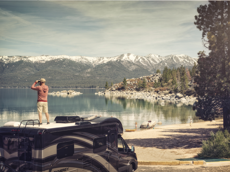 Man standing on top of motorhome using binoculars and surrounded by mountains