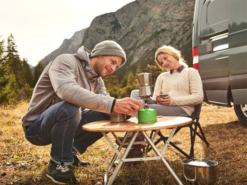 Couple turning on their camping oven while surrounded by mountains