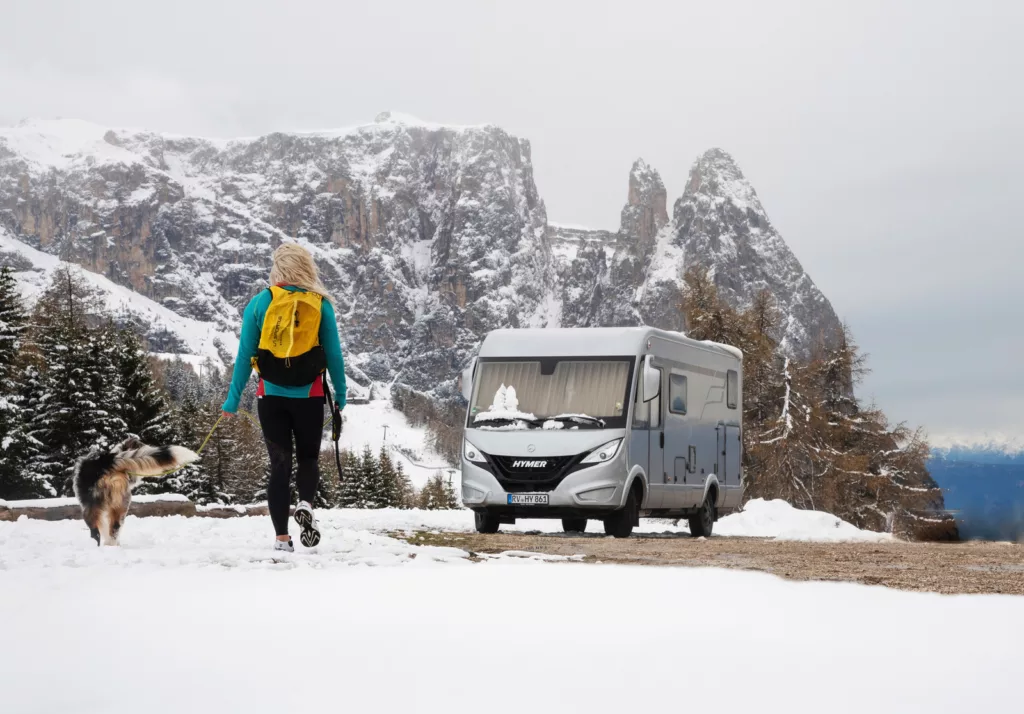 Woman hiking with dog near motorhome in the snow